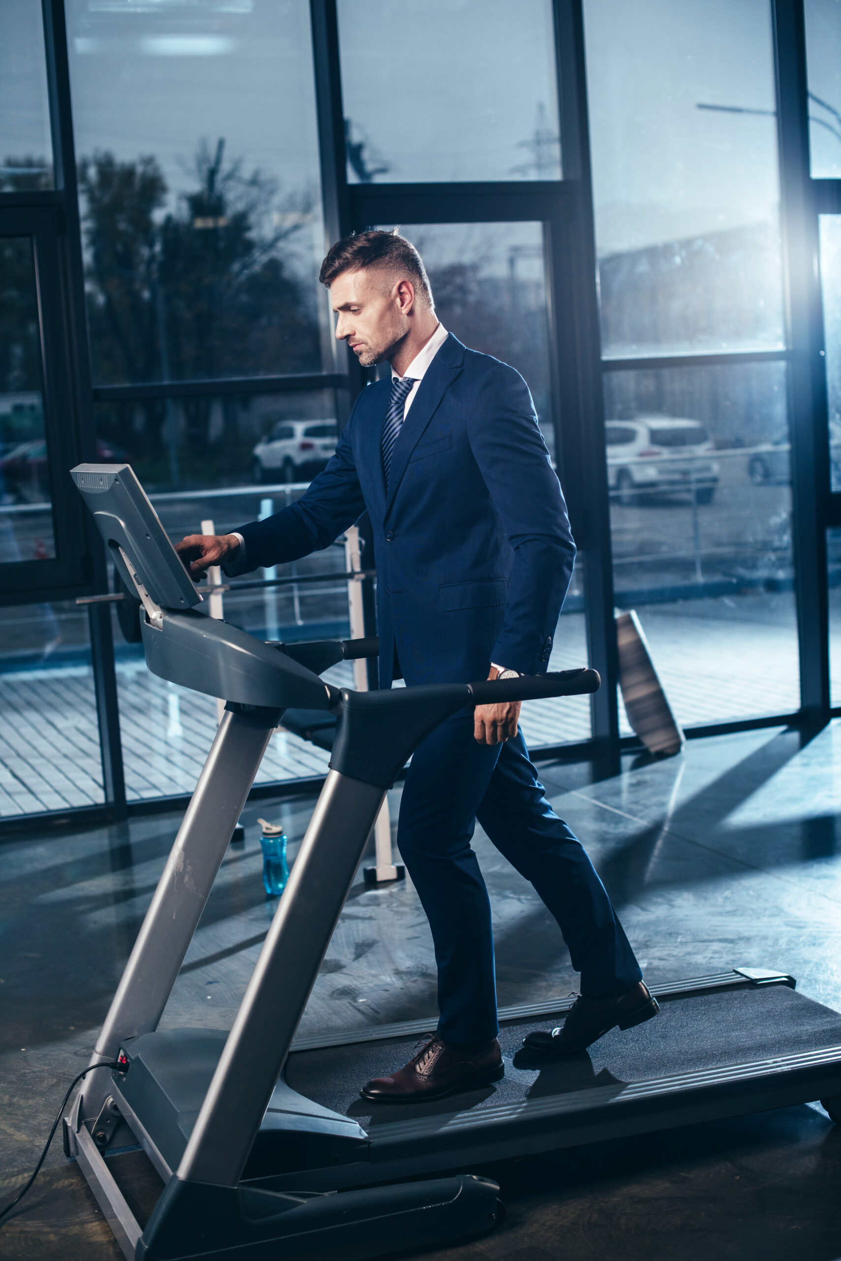 Un professionnel en costume utilise un tapis de marche au bureau pour rester actif tout en travaillant. Une illustration parfaite de l'équilibre entre santé et productivité, montrant comment intégrer l'exercice physique dans une journée de travail chargée.