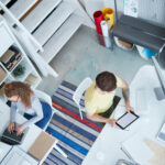 Vue aérienne d'un espace de travail moderne et créatif, mettant en scène deux professionnels concentrés sur leurs tâches respectives. Un environnement lumineux et bien organisé, idéal pour stimuler la productivité et la collaboration.